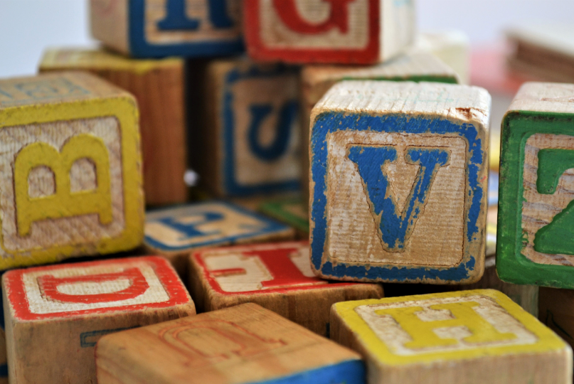 Coloured wooden alphabet blocks are stacked randomly displaying individual letters